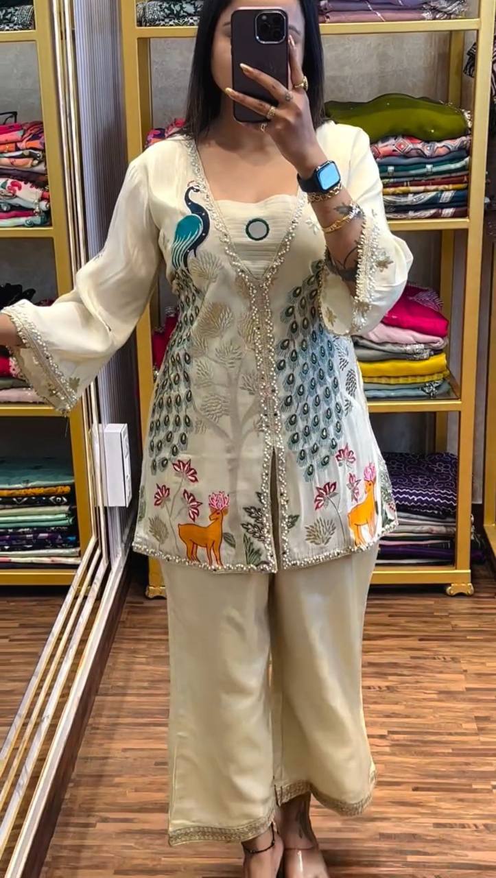 Woman wearing a cream ethnic co-ord set with heavy embroidery, peacock and deer designs, and shimmer silk fabric

